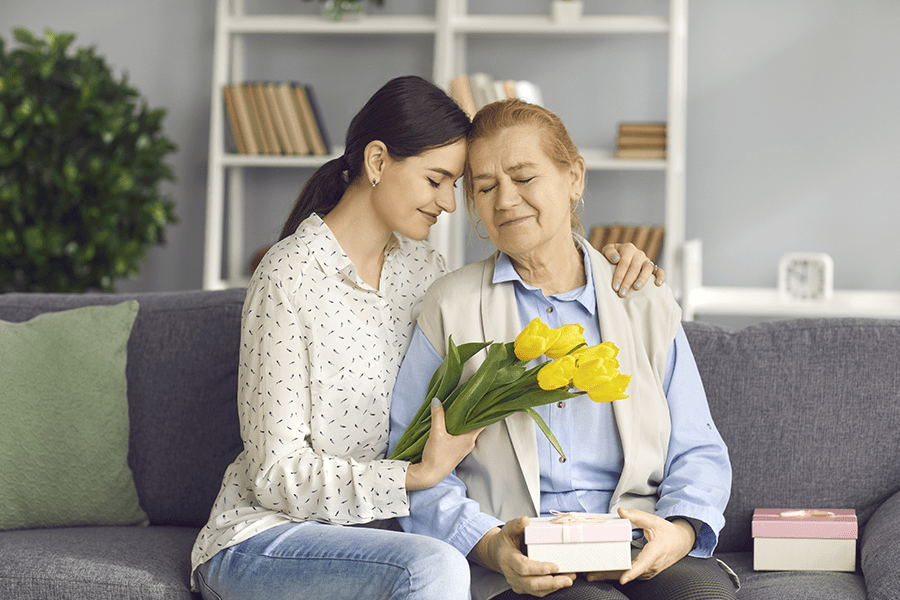 Daughter warmly presenting a bouquet of flowers to her senior mom, symbolizing the loving care and support provided in a respite care setting