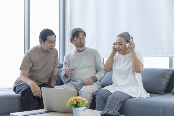 Old men and women listening to music with laptop in the living room. Senior friends group hangout, Older people meeting.