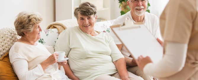 Happy elders sitting on the lounge with nurse in regards to what is respite care.